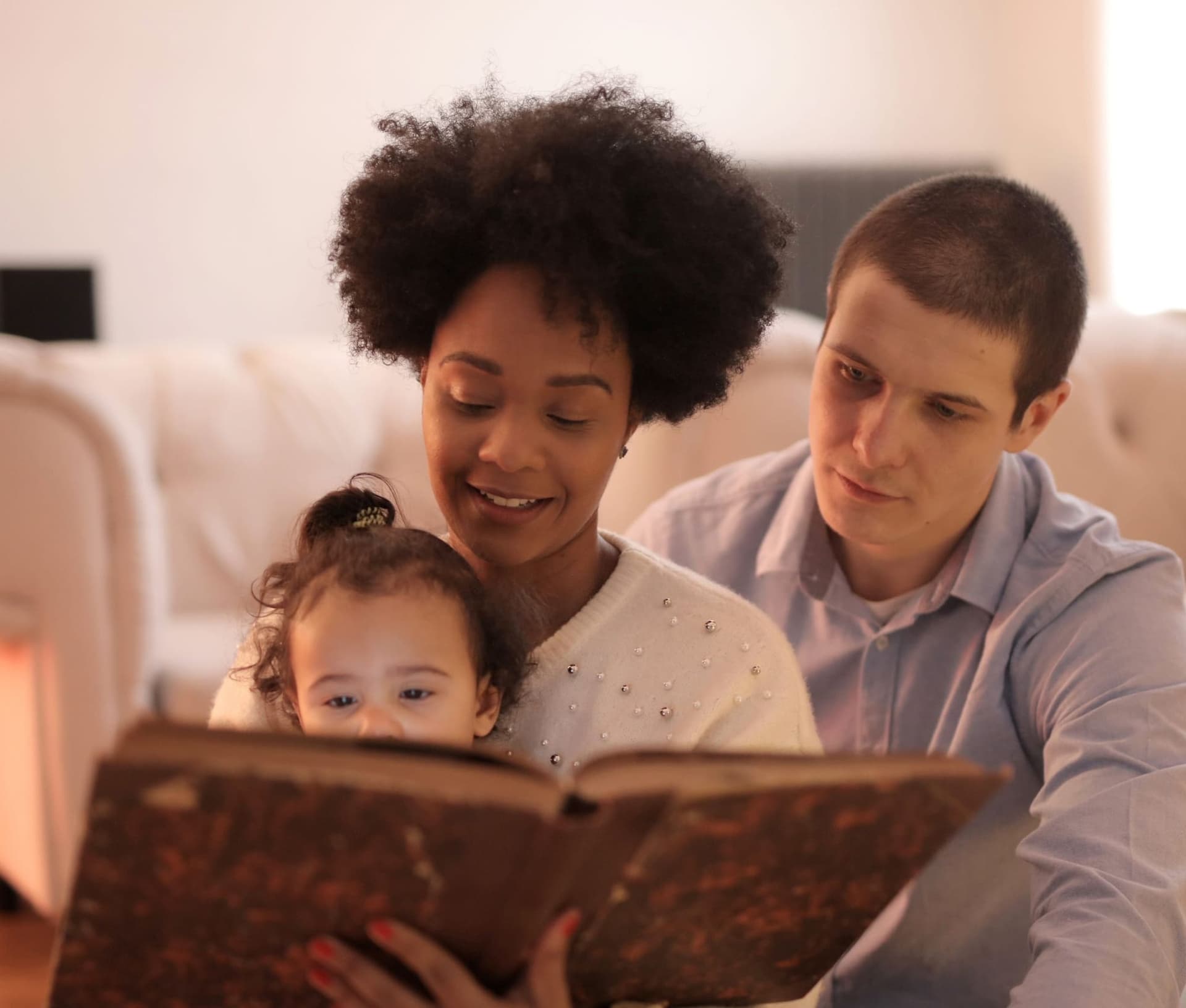 Parents lisant un livre avec leur jeune enfant dans un salon lumineux